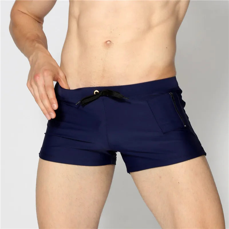 Navy blue swim shorts worn by a person on a gray background