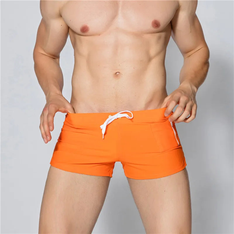 Person wearing bright orange swim shorts with a white drawstring on a plain background