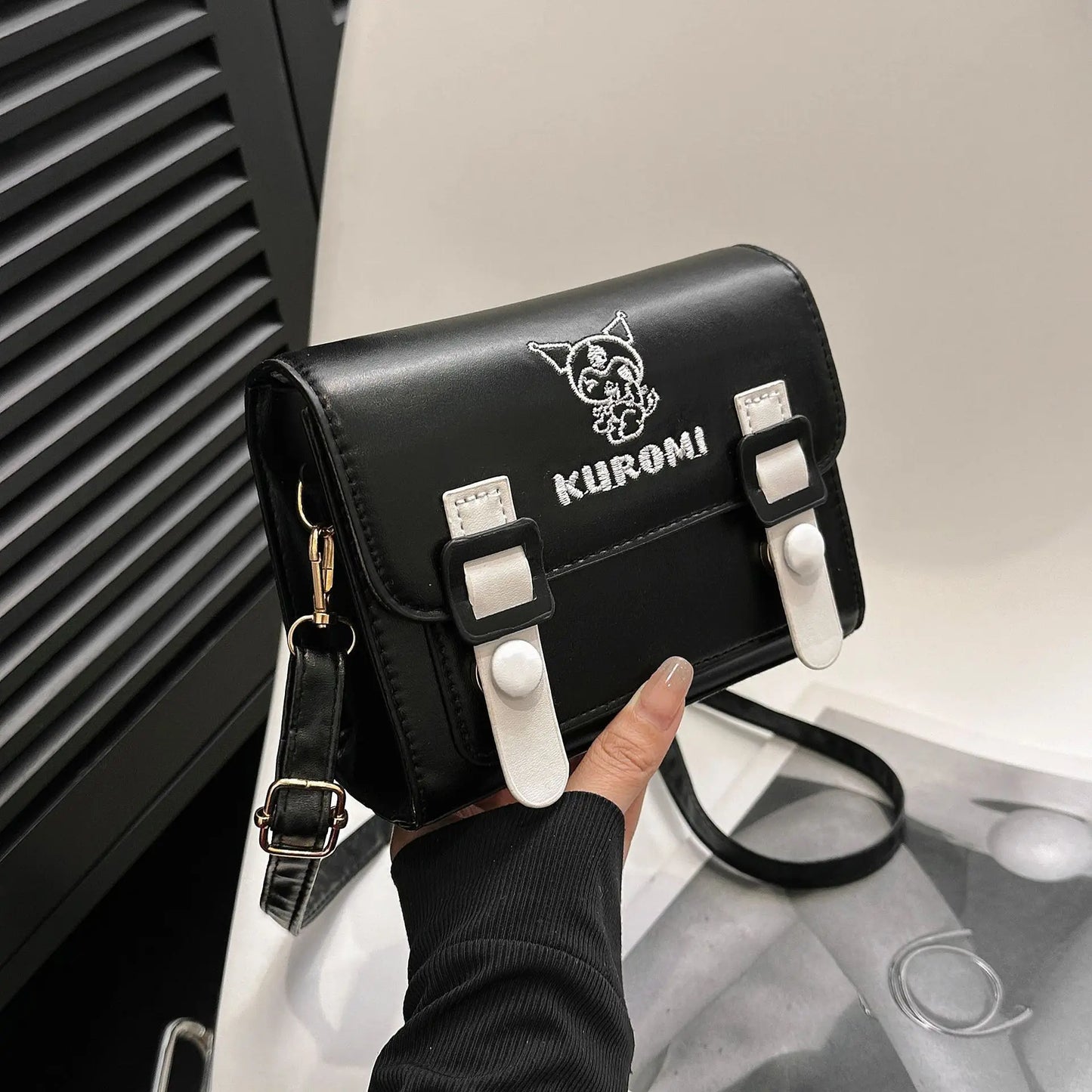 Black handbag with 'Kuromi' branding held by a person against a blurred background