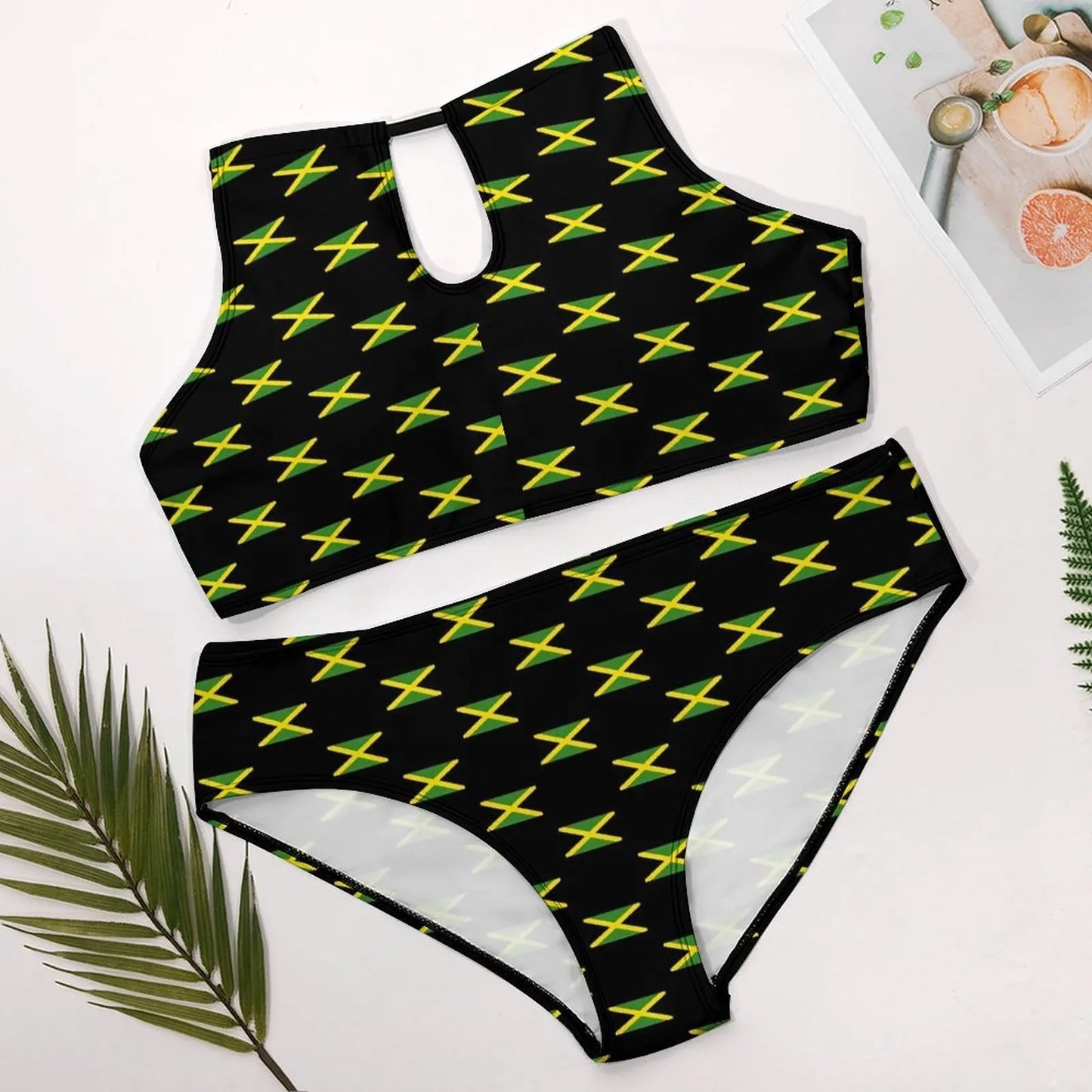 Black bikini set with yellow star pattern on a white surface with green leaves.