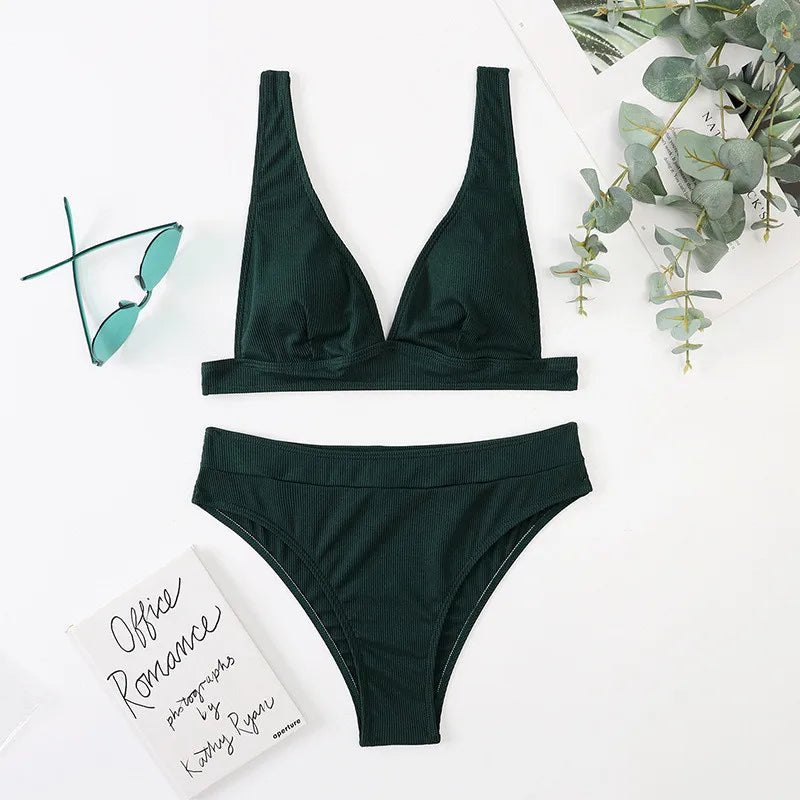 Green bikini set on a white surface with a book and eucalyptus leaves.