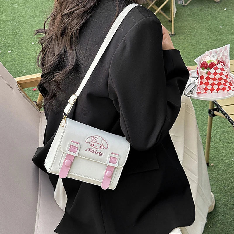 Person holding a white and pink bag with a logo, sitting outdoors on a grassy area.