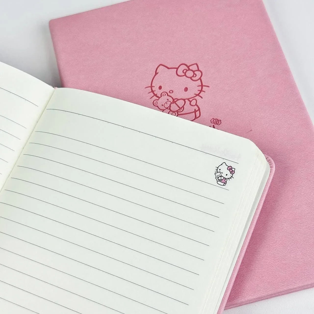 Pink notebook with Hello Kitty design and an open lined notebook on a white background