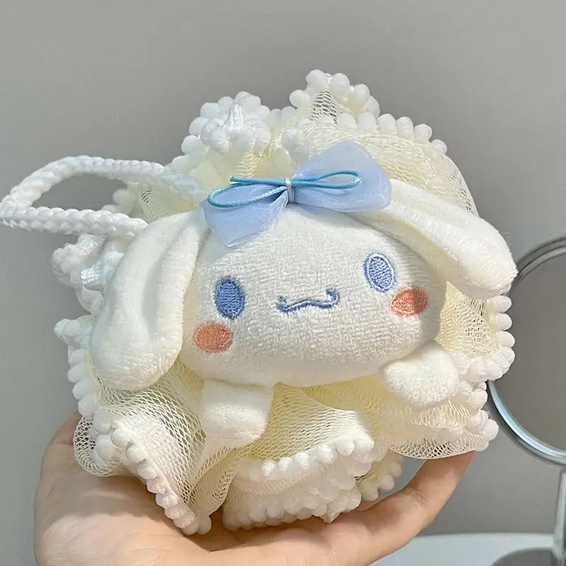 White kitty bath sponge plush toy with a blue bow held in a hand against a gray background