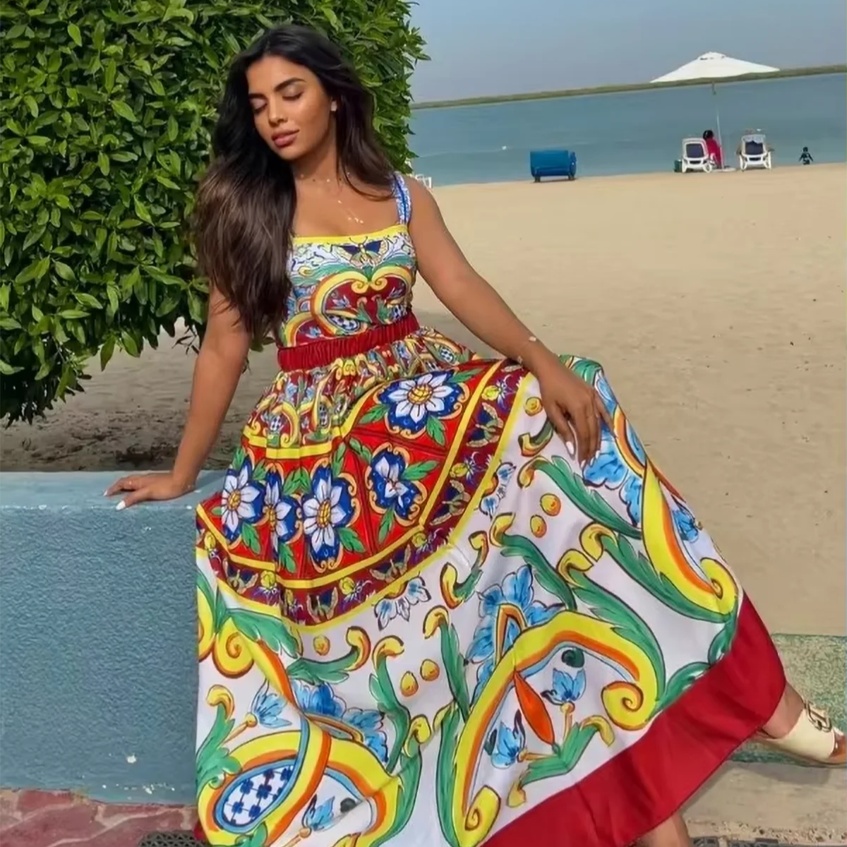 Woman in a colorful dress standing by a beach with greenery and water in the background