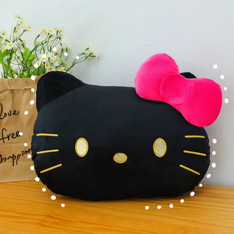 Black cat-shaped pillow with a pink bow on a wooden surface with flowers and a bag in the background.