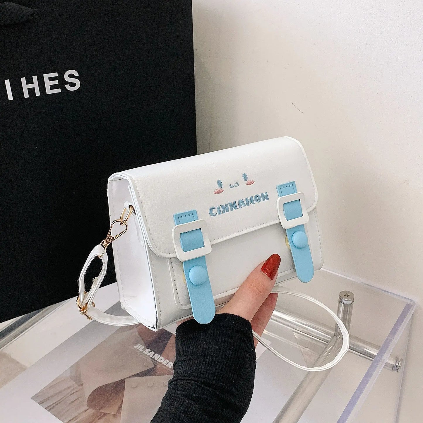 White bag with blue straps held by a hand, with a black background and 'Cinnamon' branding.