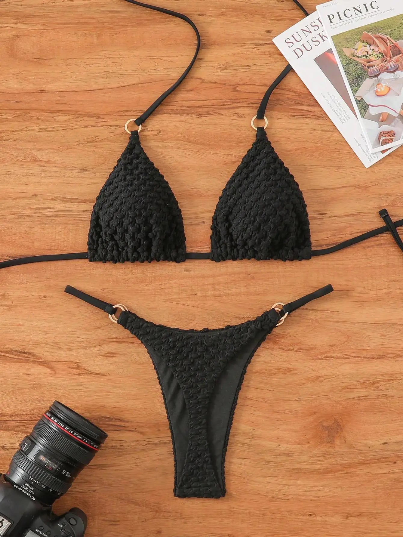 Black crochet bikini set on a wooden surface with a camera and magazine.