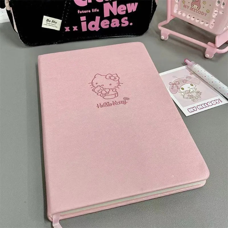 Pink notebook with Hello Kitty design on a gray surface, surrounded by stationery items.