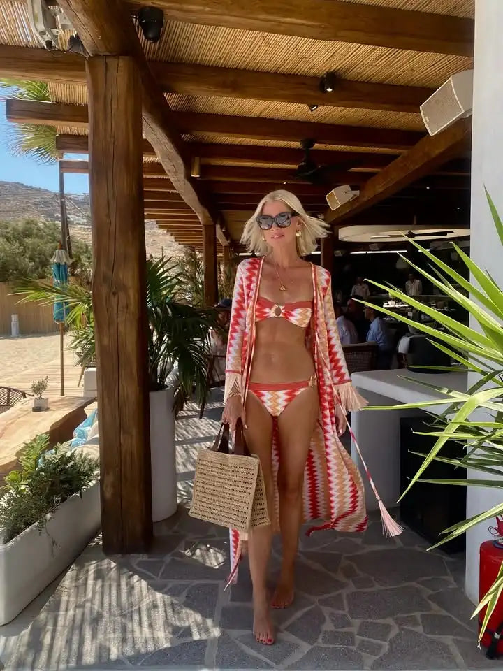 Woman in a red and white bikini with a matching cover-up standing under a wooden pergola.