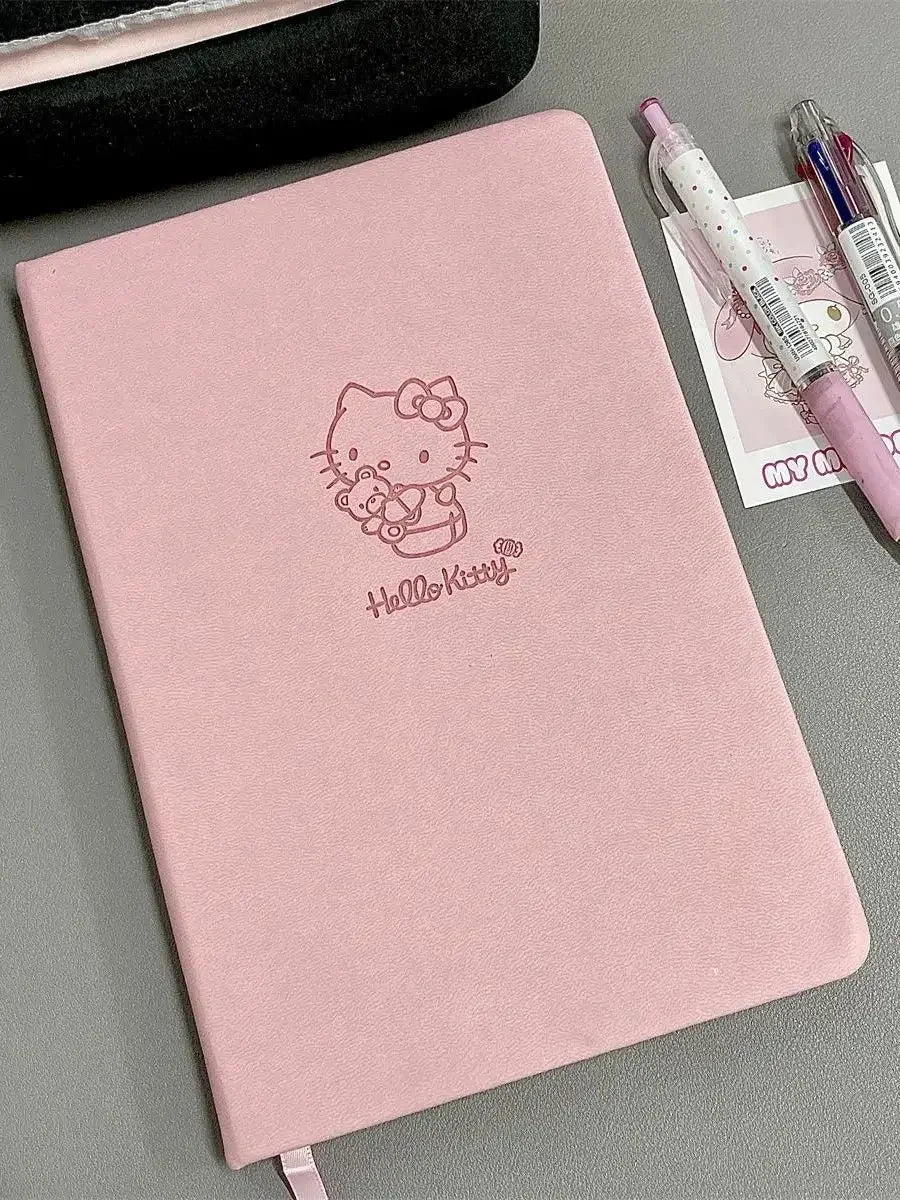 Pink notebook with Hello Kitty logo on a gray surface with pens.
