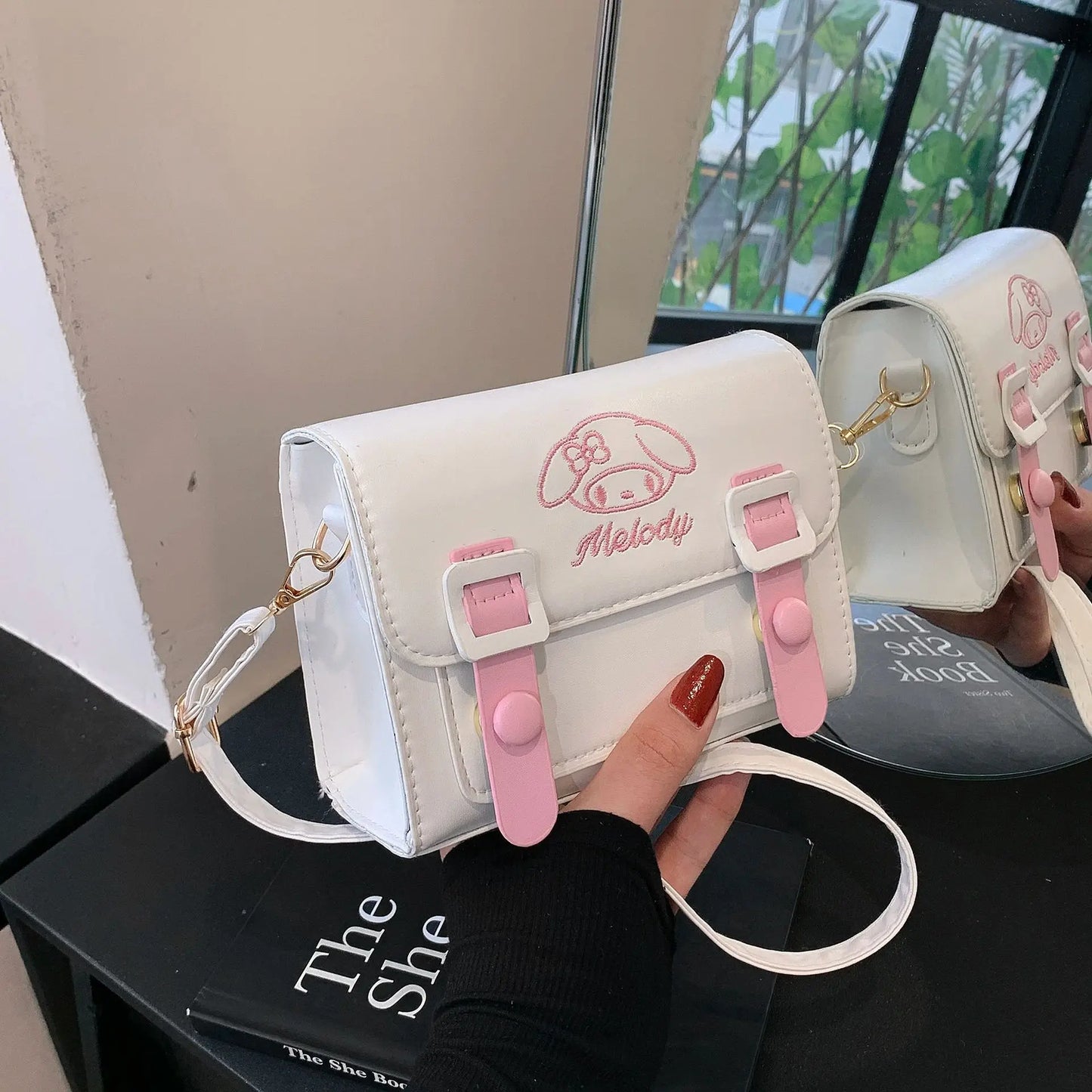 White and pink bag with 'Melody' branding held by a hand on a black surface.