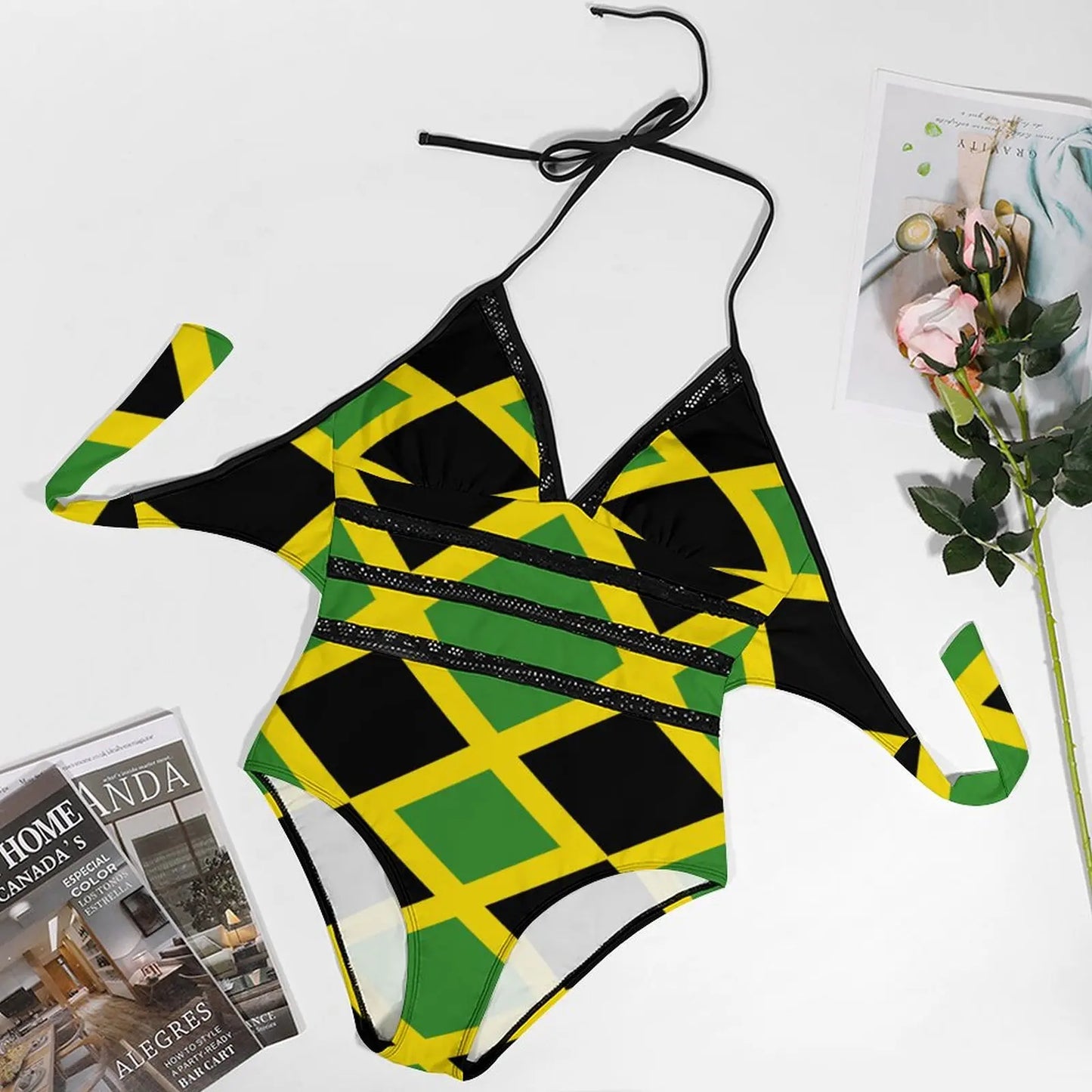 One-piece swimsuit with Jamaican flag pattern on a white surface with magazines and flowers.