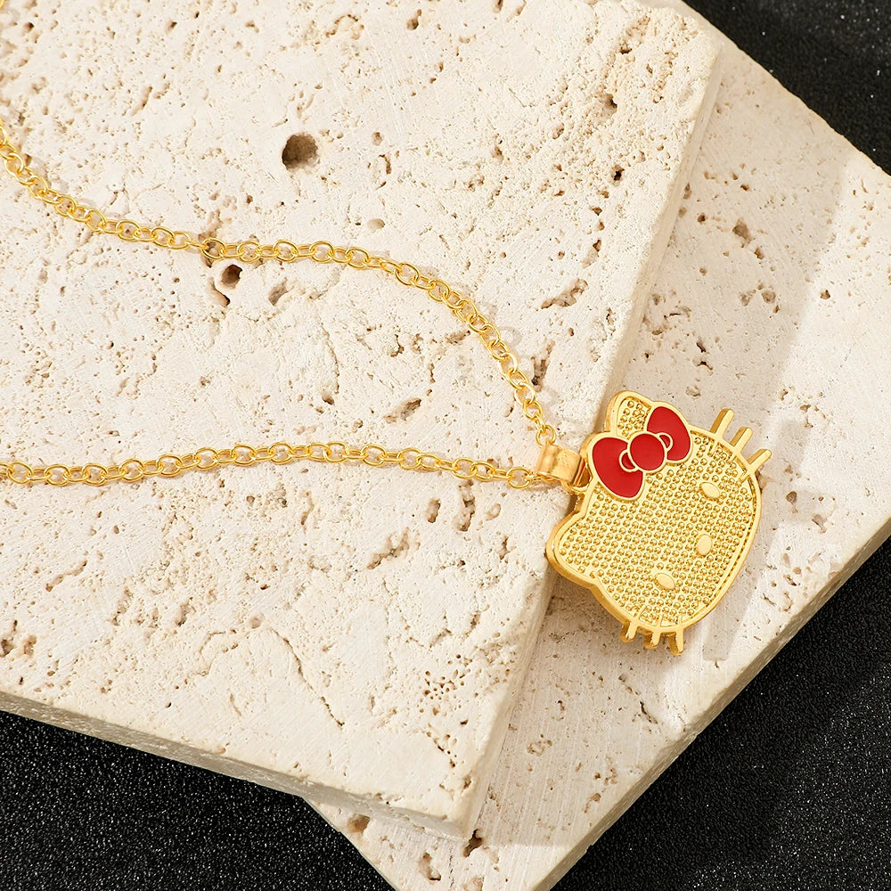 Gold necklace with a cat-shaped pendant featuring a red bow on a textured stone surface.