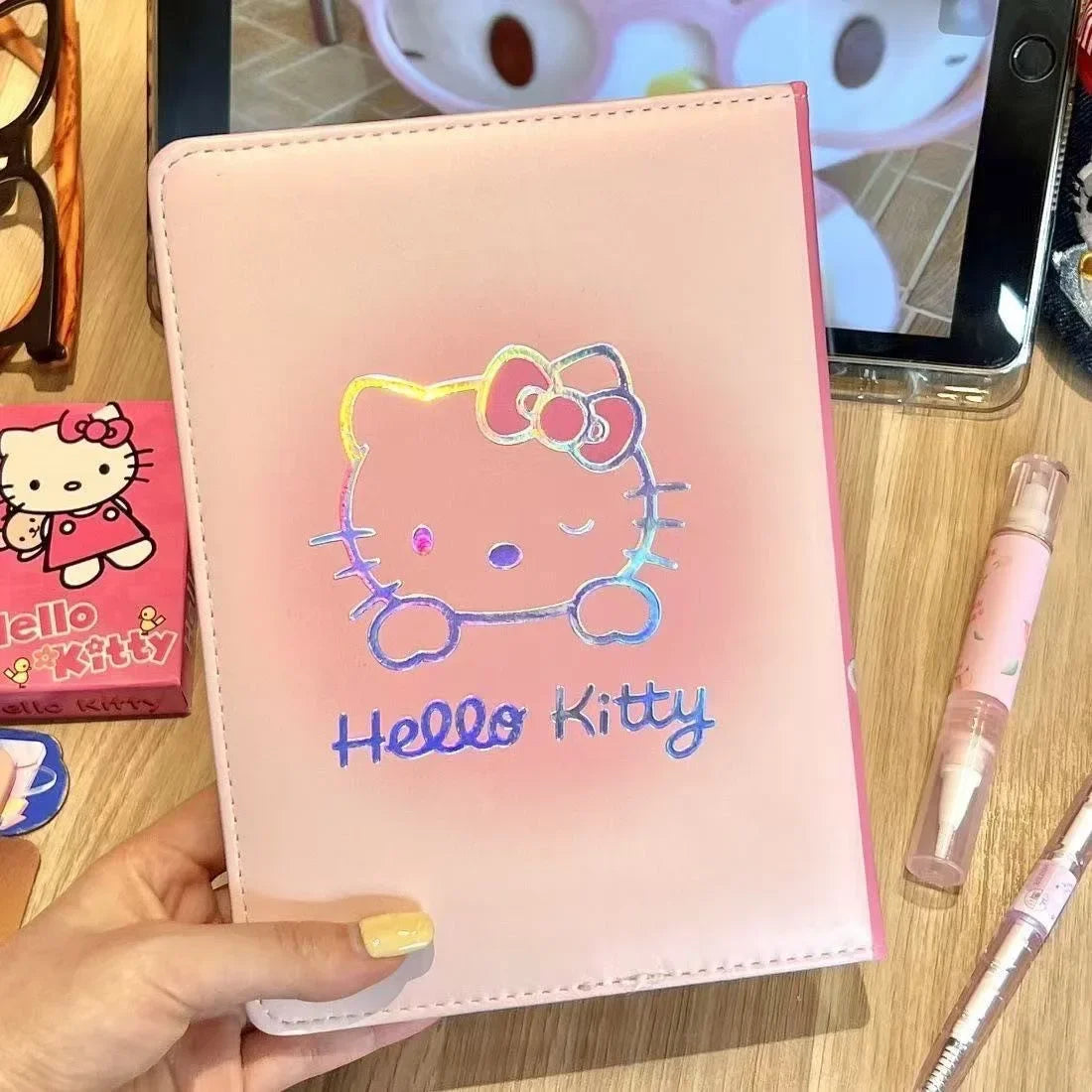 Pink Hello Kitty notebook held by a hand on a wooden surface with a blurred background.