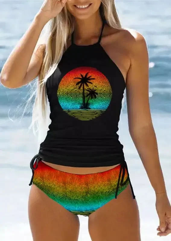 Woman wearing a black tank top with a colorful palm tree design and rainbow shorts by the water.