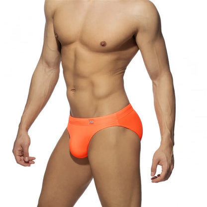 Man wearing bright orange swim briefs on a white background