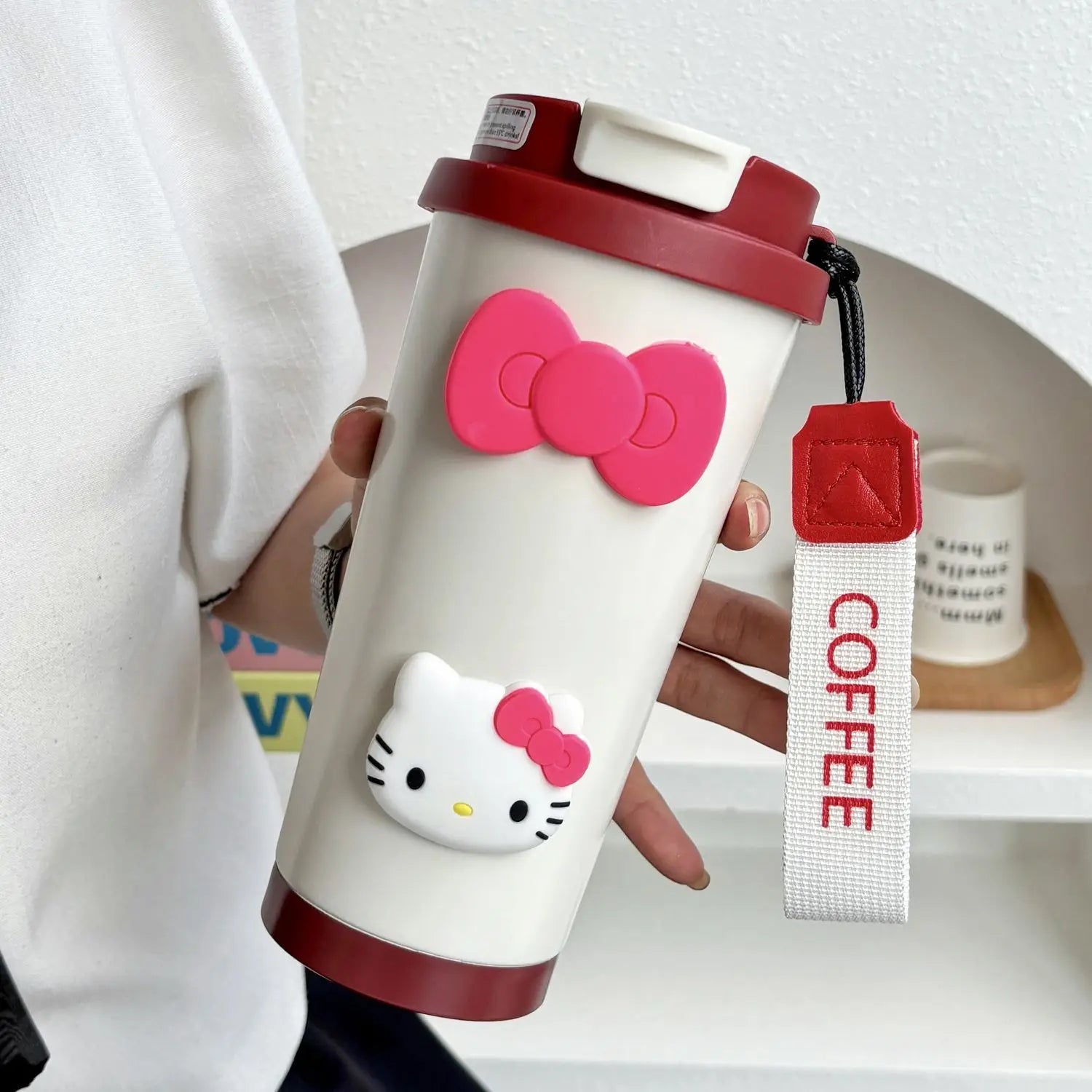 Hello Kitty-themed coffee tumbler with a red bow and 'COFFEE' tag, held by a person.