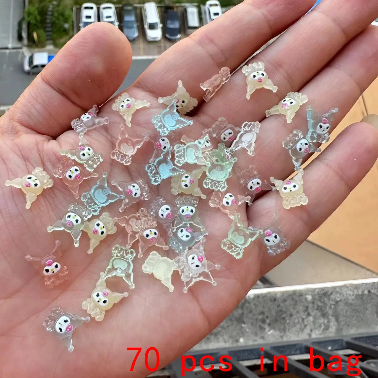 Hand holding small transparent figurines with cartoon faces, labeled '70 pcs in bag'.