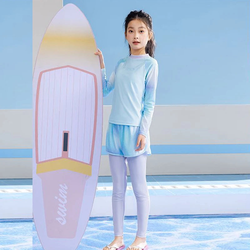 Young girl in a light blue swimsuit standing next to a surfboard with a blue background