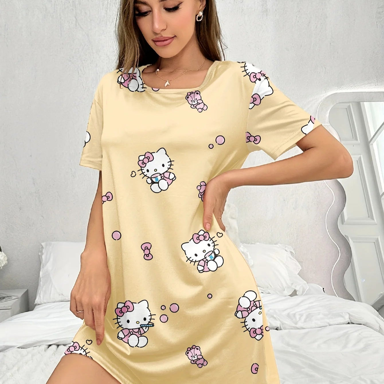Woman wearing a yellow nightshirt with Hello Kitty prints in a bedroom setting.