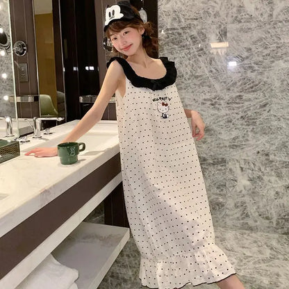 Woman in a white polka dot dress with black collar standing in a bathroom.