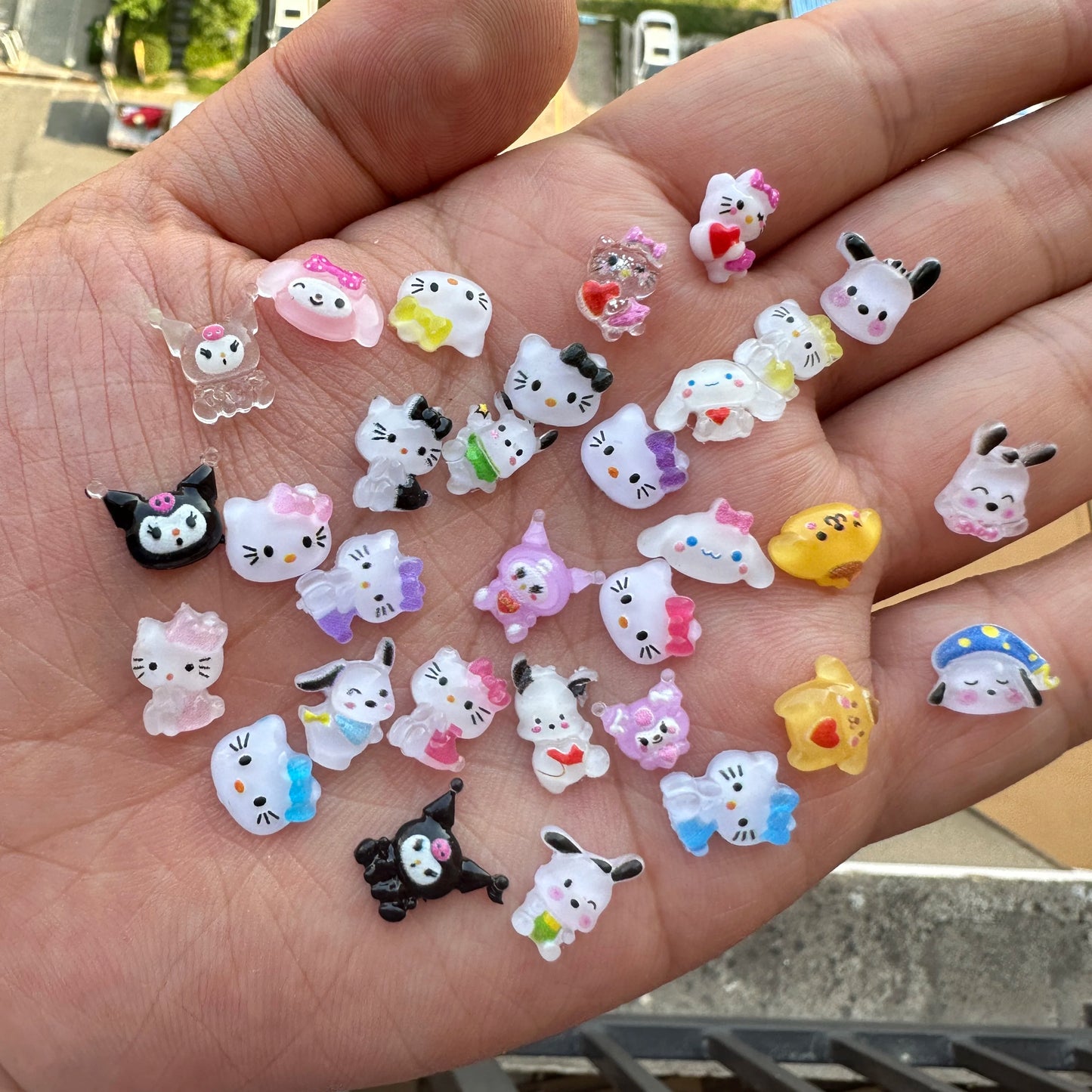 Hand holding various small cartoon character figurines on a blurred outdoor background
