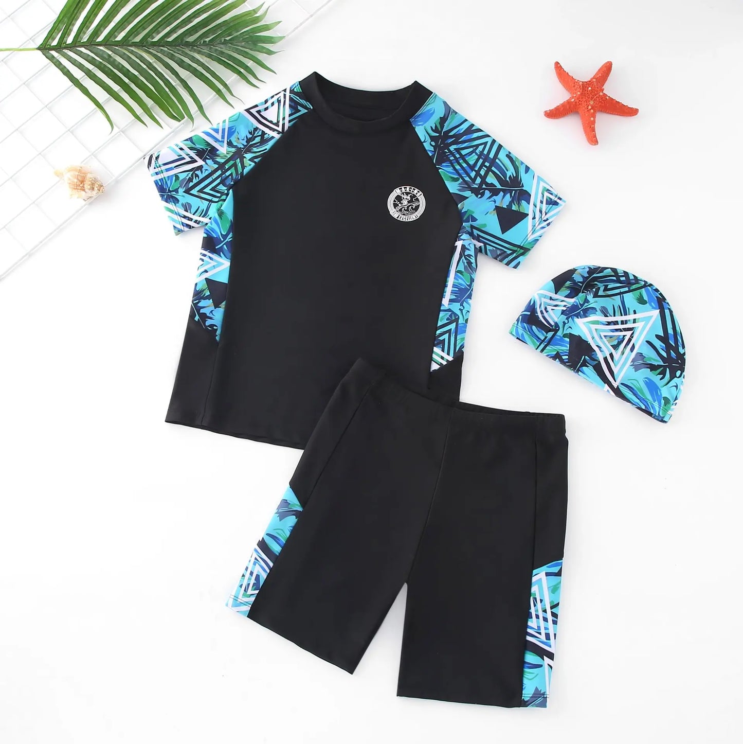Children's swim set with black and blue patterned rash guard and shorts, accompanied by a matching cap on a white background.