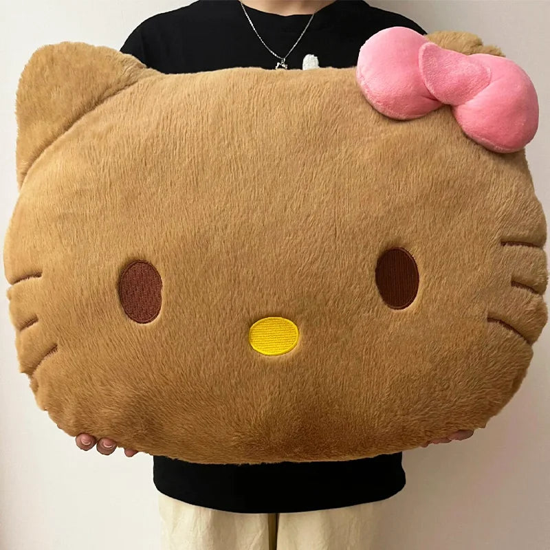Large plush pillow shaped like a cat face with a pink bow held by a person.
