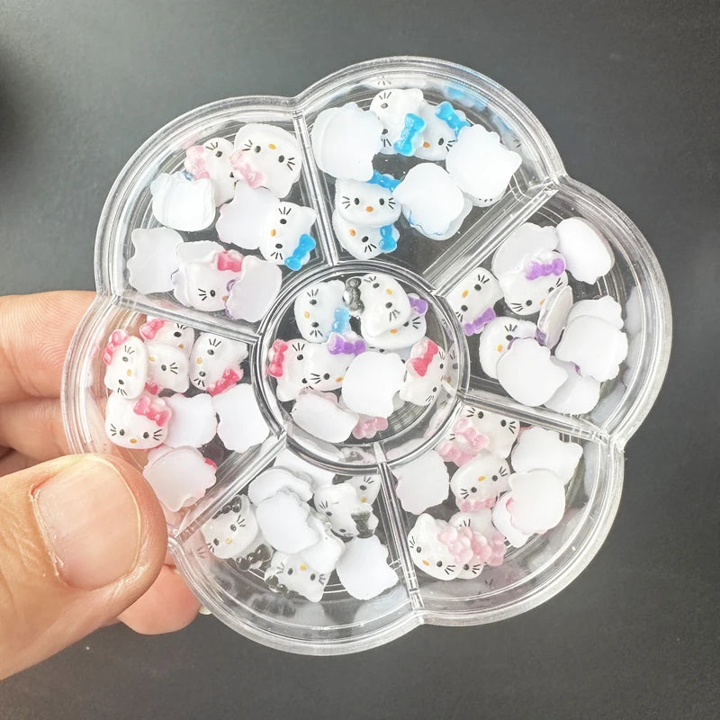 Clear plastic container with compartments filled with small white cat-shaped objects, held by a hand against a dark background.