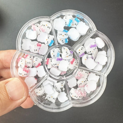 Clear plastic container with compartments filled with small white cat-shaped objects, held by a hand against a dark background.
