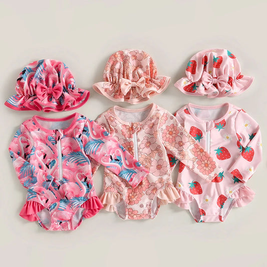 Set of pink children's swimwear and hats with floral and strawberry patterns on a light gray background.