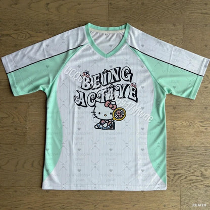 White and green sports jersey with 'Being Active' text and Hello Kitty graphic on a wooden surface