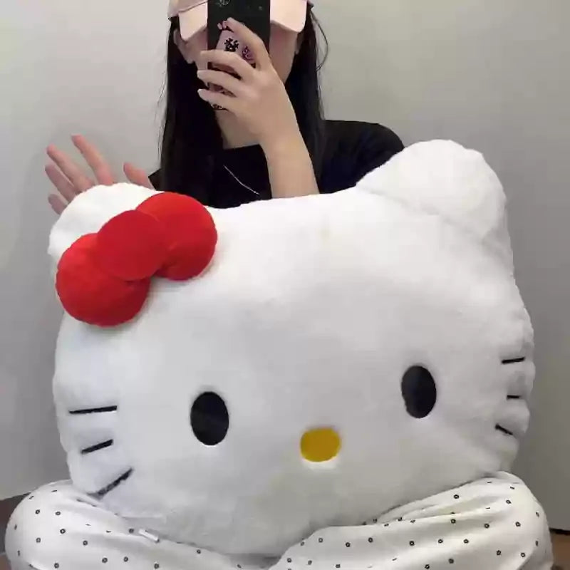 Person holding a large white plush toy pillow shaped like a cat face with a red bow.