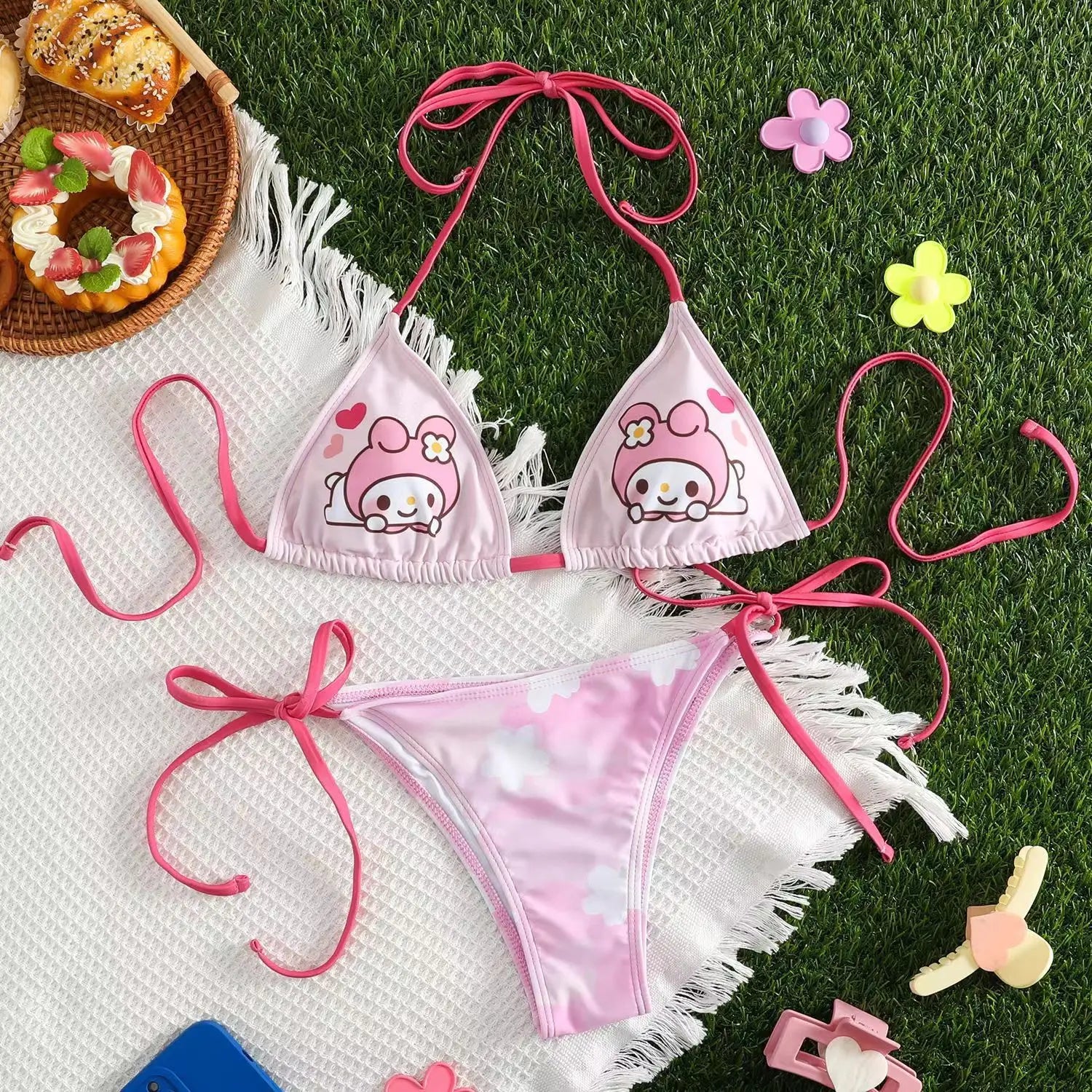 Pink bikini set with cartoon character design on grass with donuts and flowers.