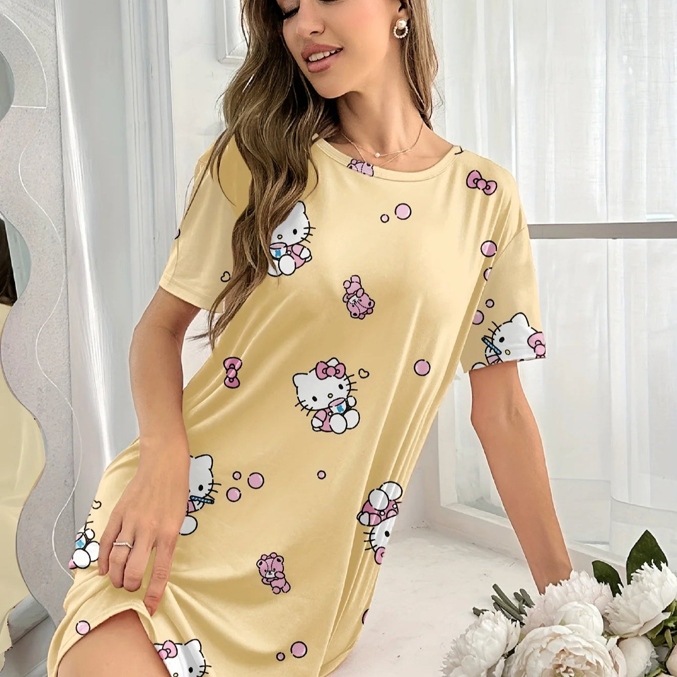 Woman wearing a yellow nightgown with Hello Kitty patterns in a bright room.