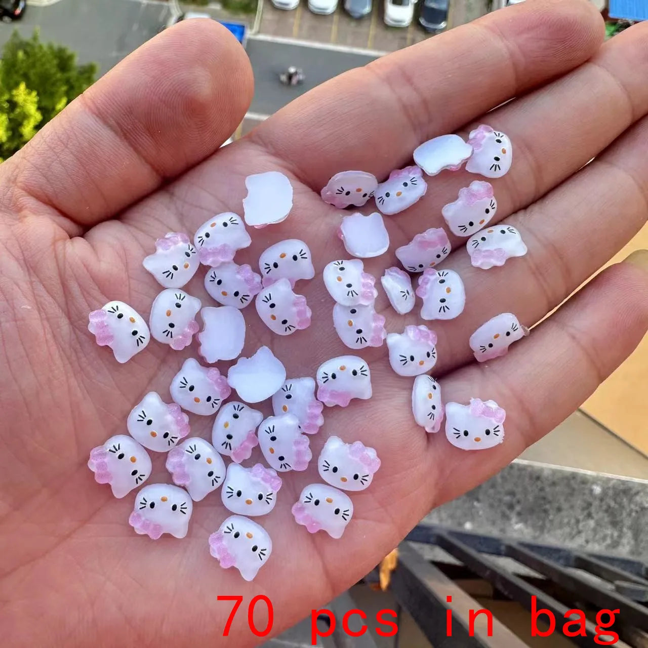 Hand holding small cat-shaped figurines with pink accents, labeled '70 pcs in bag'.