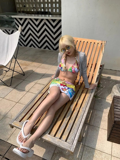 Woman in a colorful bikini and gray cardigan lying on a wooden bench outdoors.