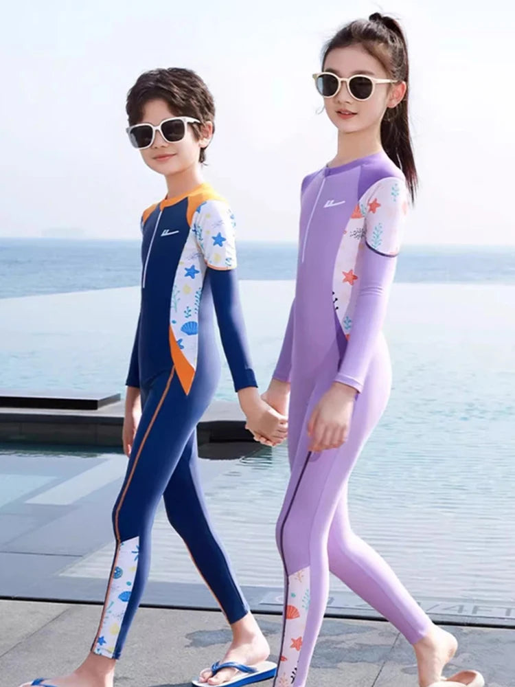 Two children in colorful wetsuits standing by a pool with ocean view.