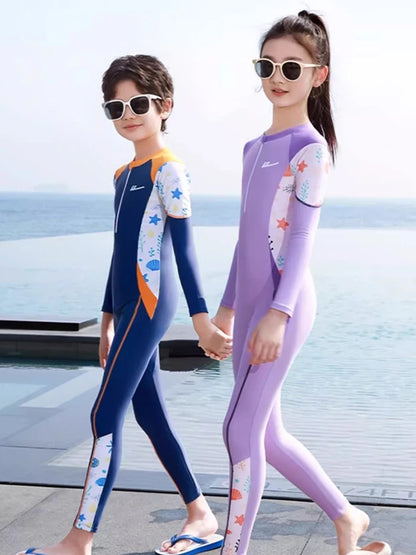 Two children in colorful wetsuits standing by a pool with ocean view.