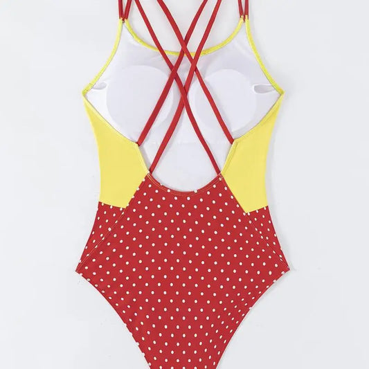 One-piece swimsuit with red polka dot pattern and yellow and red criss-cross straps on a white background