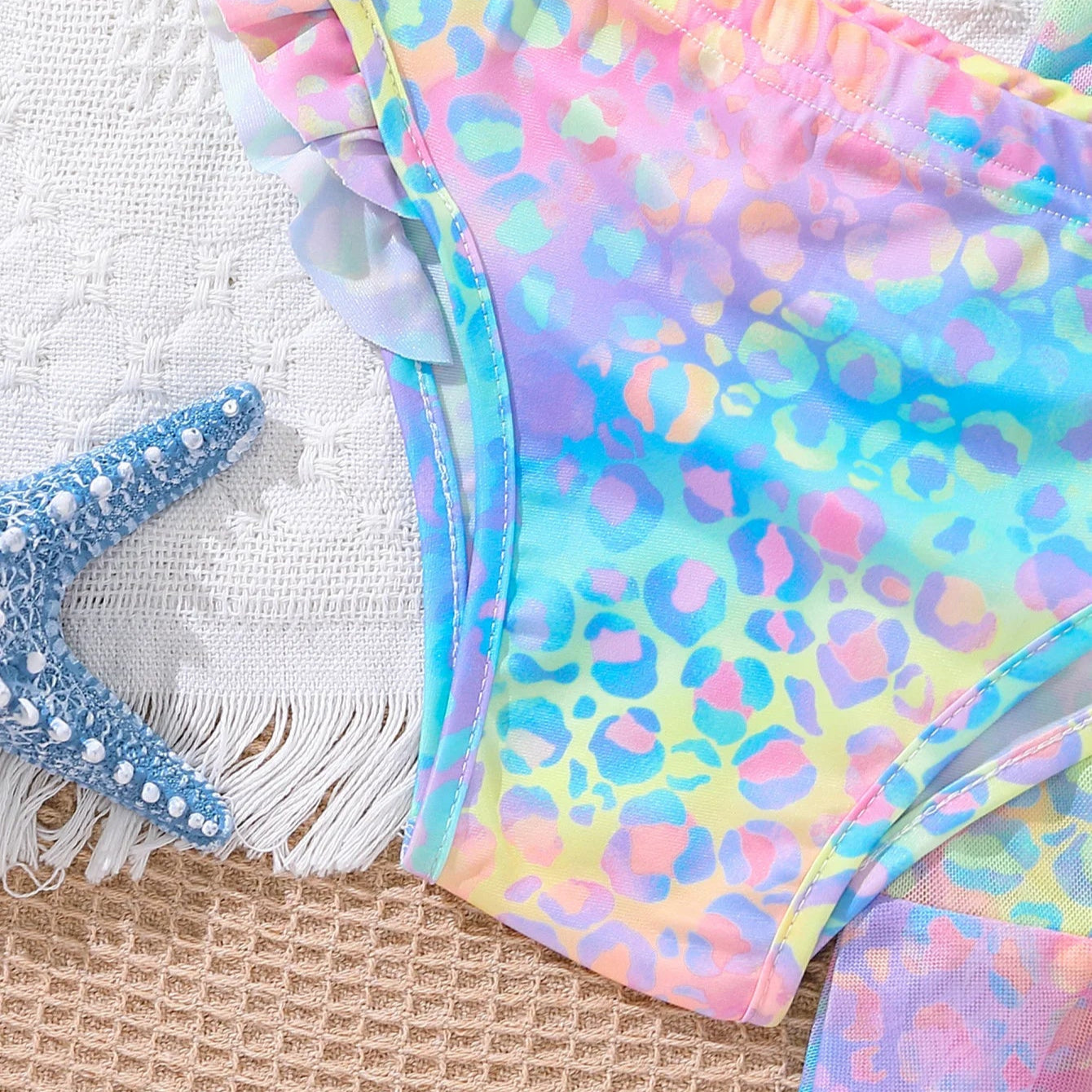Colorful leopard print bikini with ruffled edges on a textured surface.