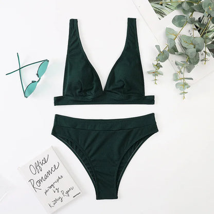Green bikini set on a white surface with a book and eucalyptus leaves.