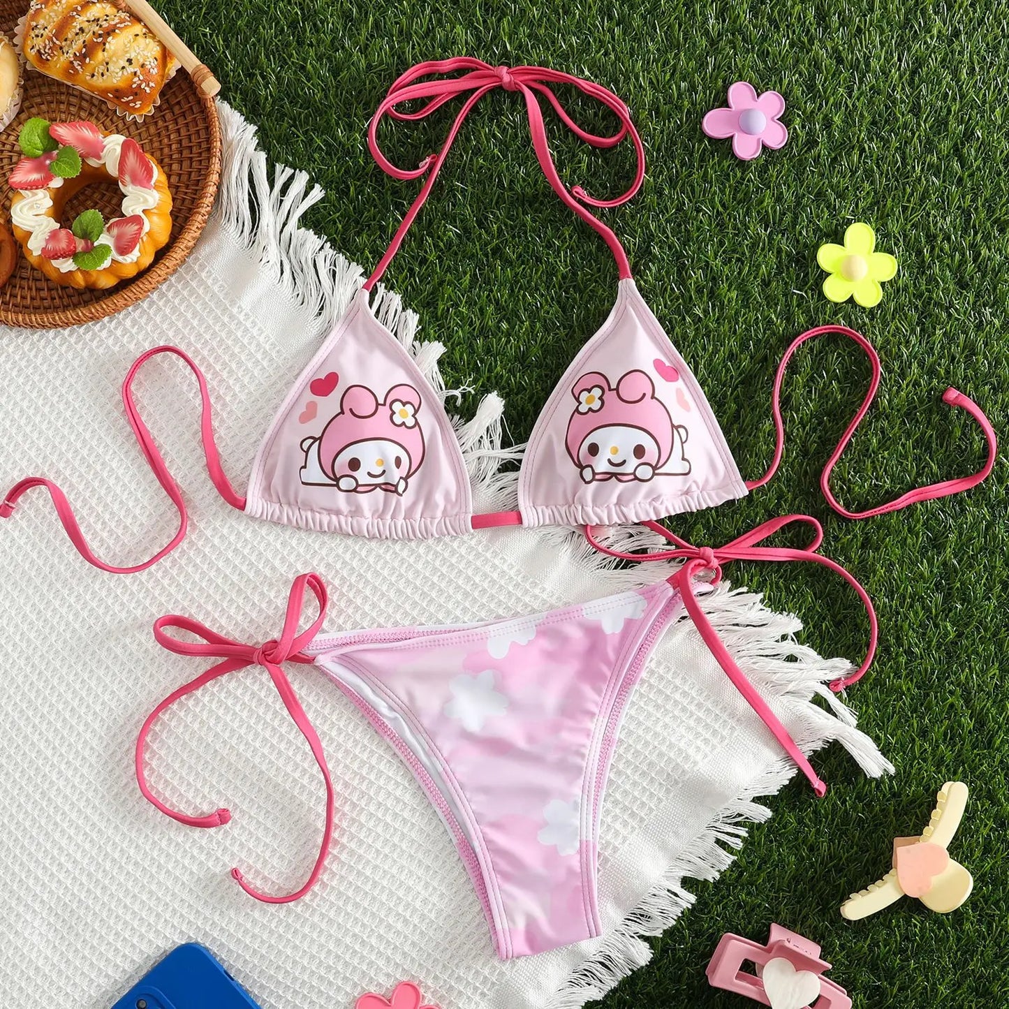 Pink bikini set with cartoon character design on grass with donuts and flowers.