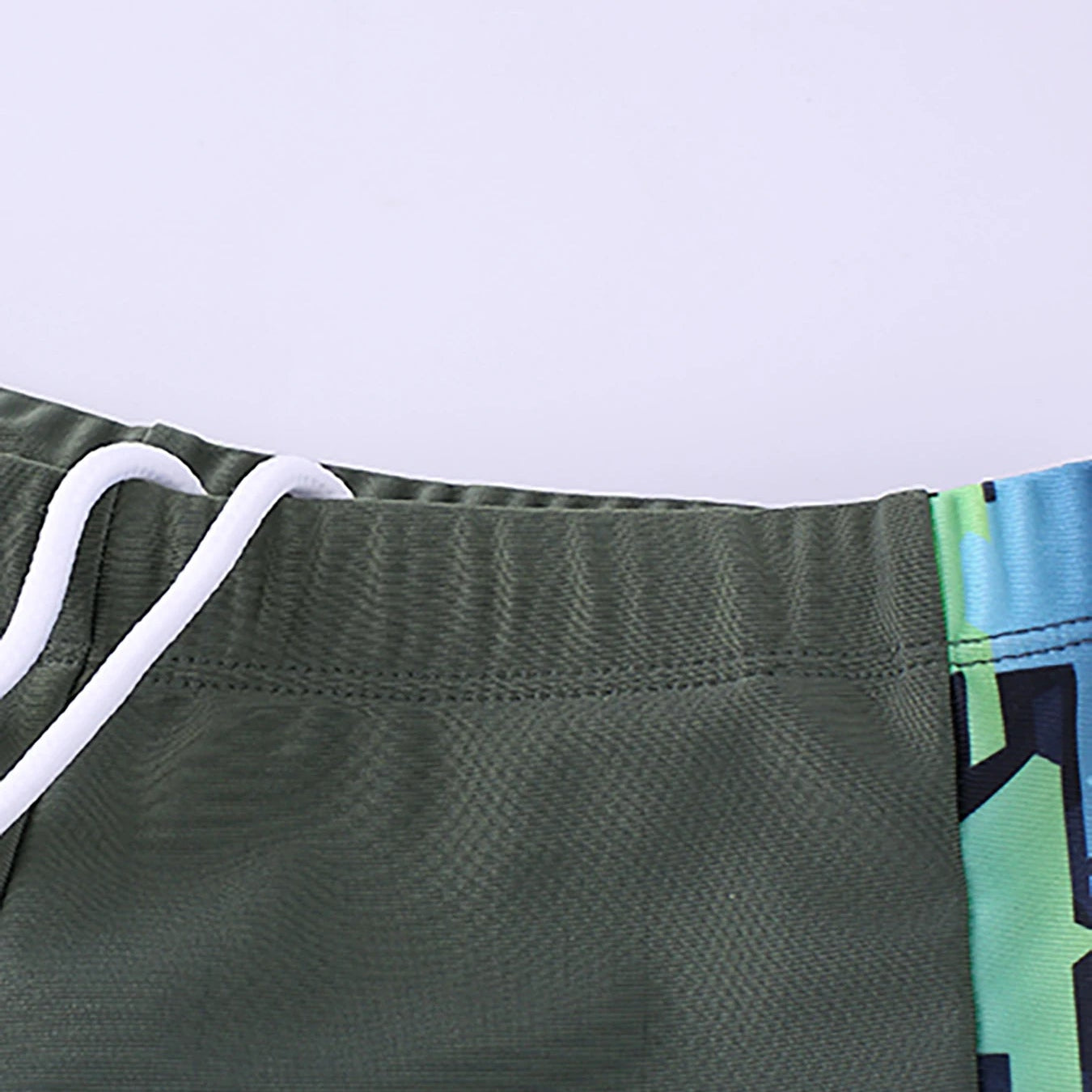 Close-up of a green athletic shorts with a white drawstring on a light purple background