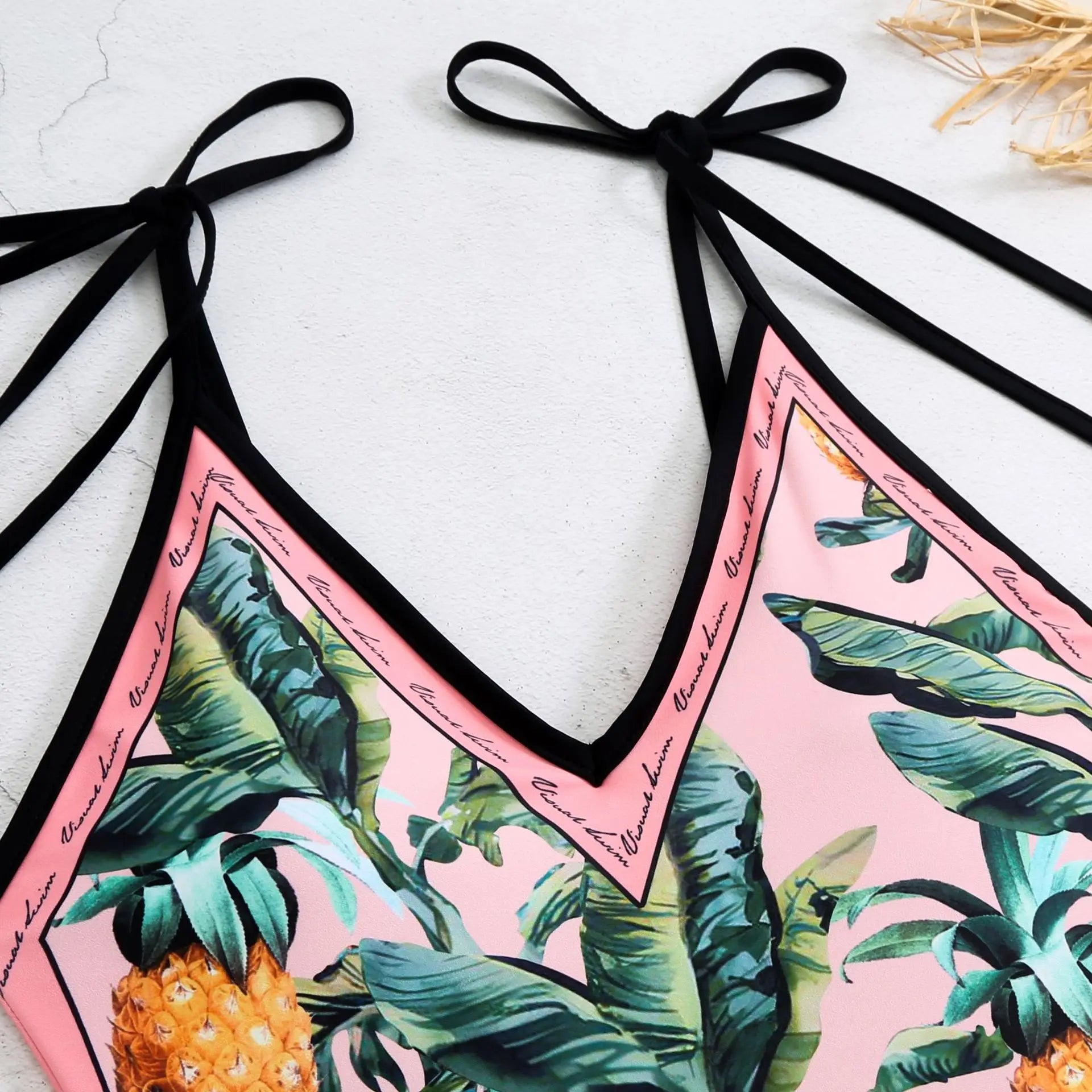 Tropical-themed bikini set with pink background and black straps on a light surface.