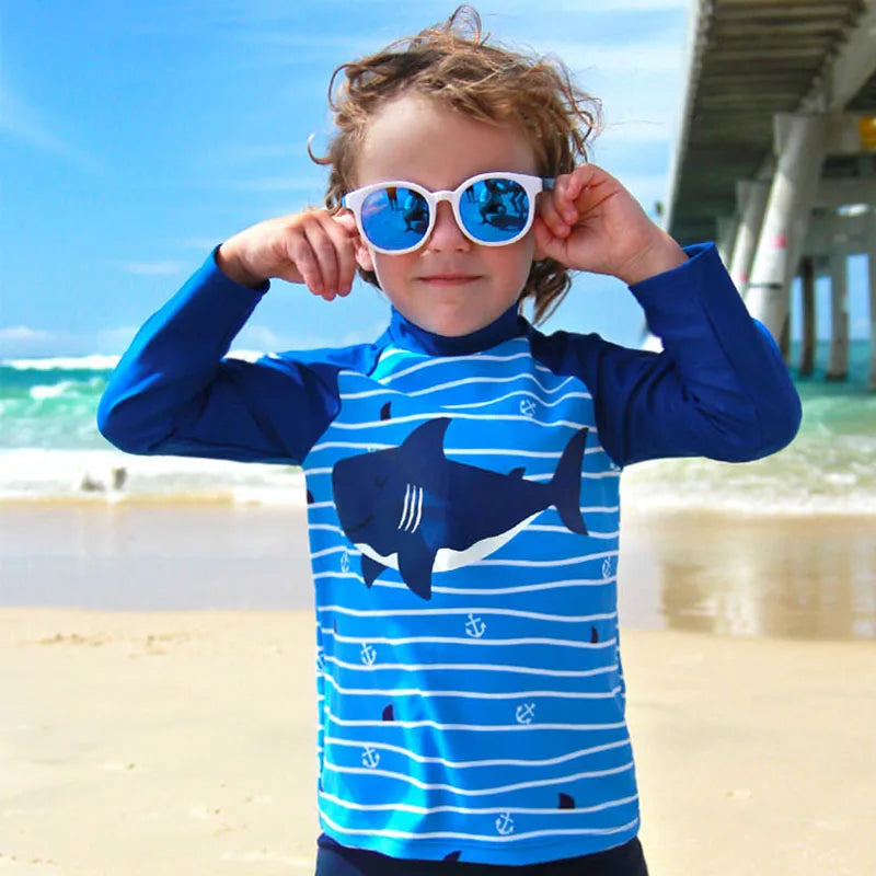 Child wearing a blue and white striped shirt with shark design on a beach