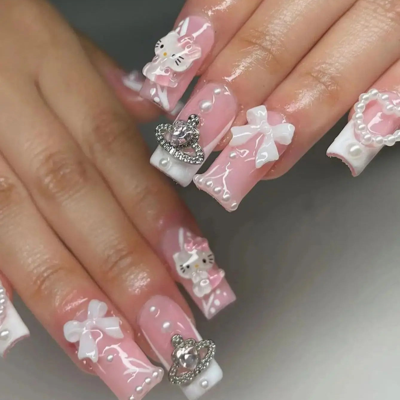 Nails with pink and white designs, including bows and heart shapes, on a neutral background.