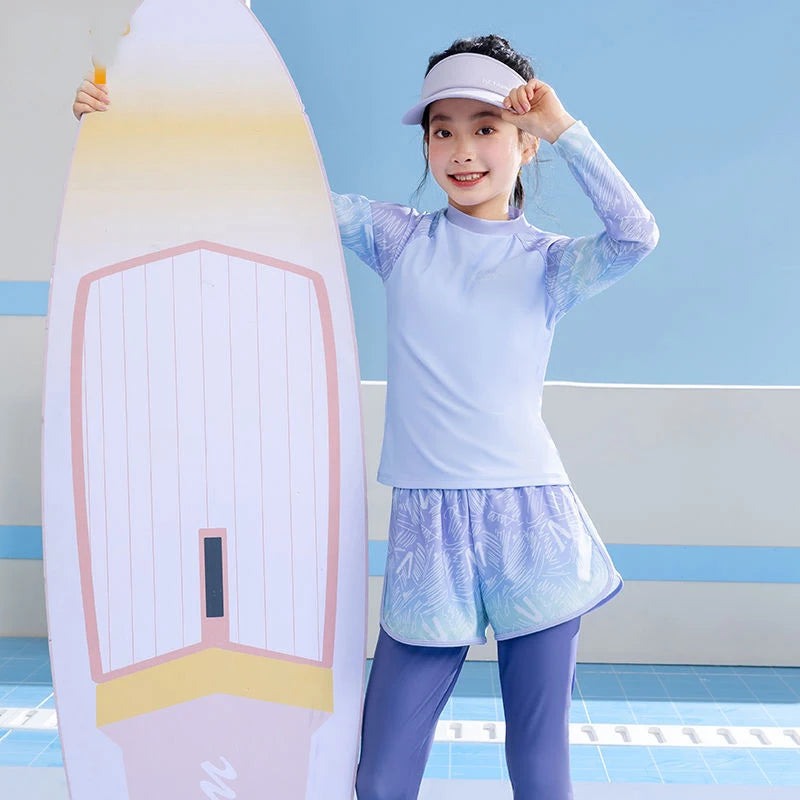 Child in light blue long-sleeve top and shorts standing next to a colorful surfboard on a pool deck.