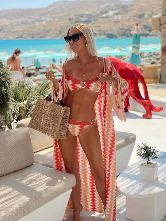 Woman in a red and white striped bikini with a matching cover-up standing by a poolside with a scenic background.